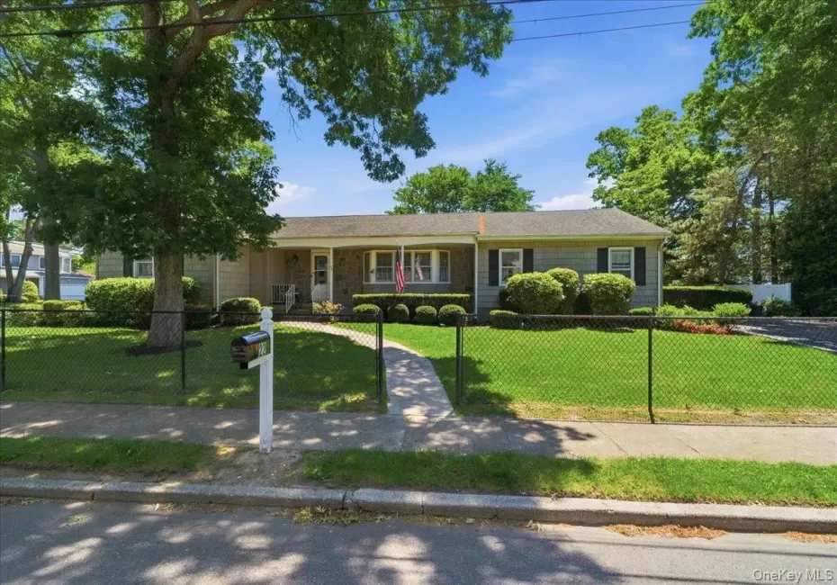 Ranch-style residence featuring a well-maintained lawn, mature trees, and a black chain-link fence Ranch-style residence featuring a well-maintained lawn, mature trees, and a black chain-link fence