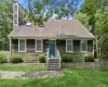 Shingle-sided residence featuring a prominent chimney, an entryway with steps and railings, and a blue door Shingle-sided residence featuring a prominent chimney, an entryway with steps and railings, and a blue door