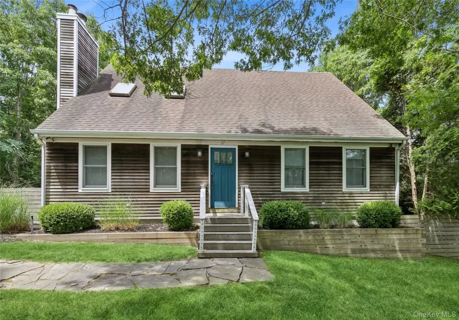 Shingle-sided residence featuring a prominent chimney, an entryway with steps and railings, and a blue door Shingle-sided residence featuring a prominent chimney, an entryway with steps and railings, and a blue door