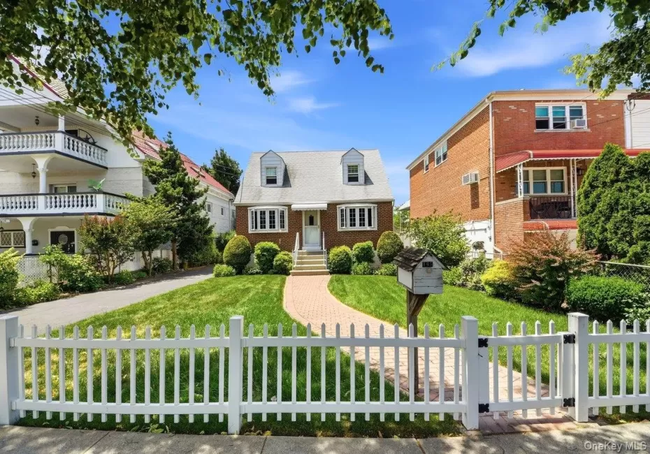 Brick exterior home featuring a gabled roof, white picket fence, and a curved brick pathway Brick exterior home featuring a gabled roof, white picket fence, and a curved brick pathway