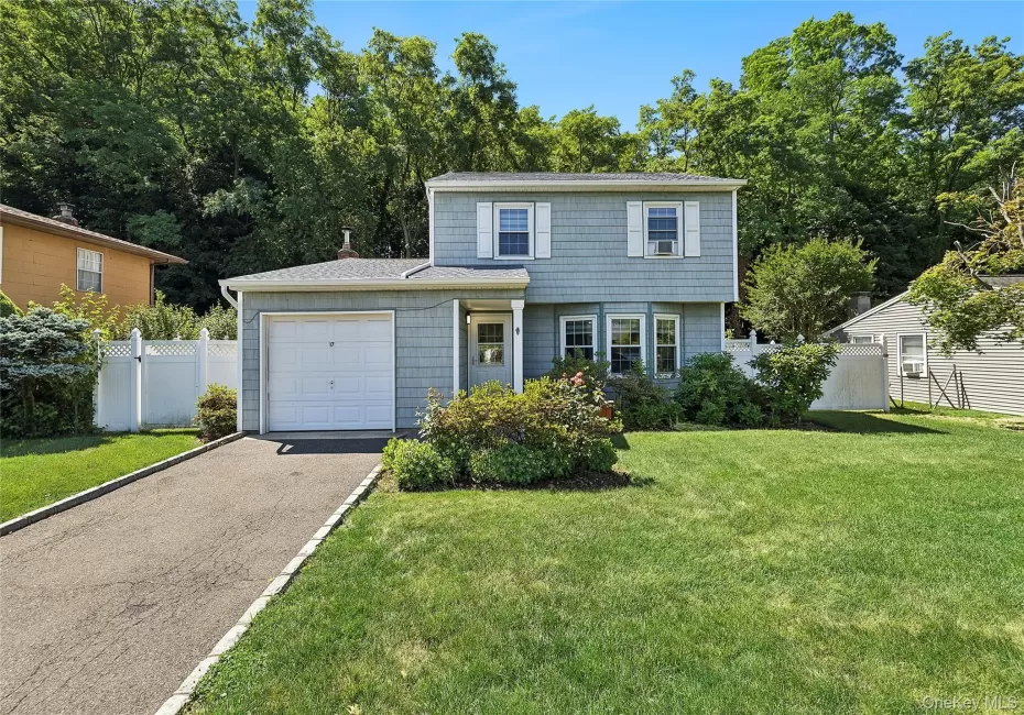 Two-story residence featuring light blue siding with white trim, a one-car garage, and a paved driveway with stone border Two-story residence featuring light blue siding with white trim, a one-car garage, and a paved driveway with stone border