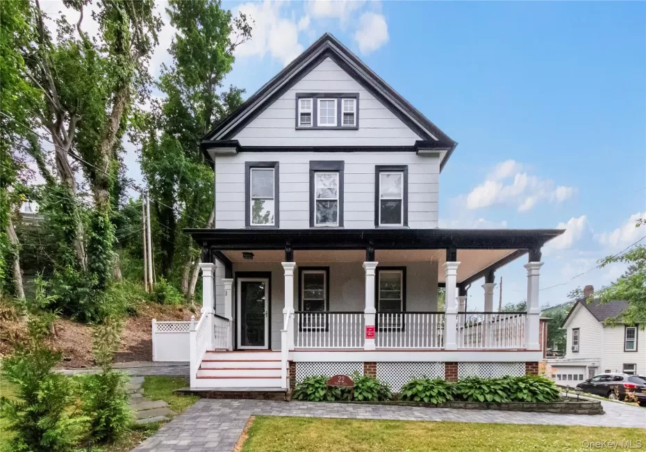 Two-story residence featuring a covered front porch with white columns, light gray siding, dark trim, and a gabled roofline Two-story residence featuring a covered front porch with white columns, light gray siding, dark trim, and a gabled roofline