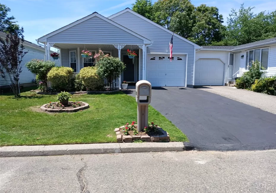Ranch-style exterior with light blue siding, a covered porch with white lattice detailing, an attached garage, a second garage or storage area, and a manicured lawn with established landscaping Ranch-style exterior with light blue siding, a covered porch with white lattice detailing, an attached garage, a second garage or storage area, and a manicured lawn with established landscaping