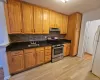 Kitchen featuring stainless steel gas range, dark stone counters, freestanding refrigerator, light wood finished floors, and brown cabinets Kitchen featuring stainless steel gas range, dark stone counters, freestanding refrigerator, light wood finished floors, and brown cabinets