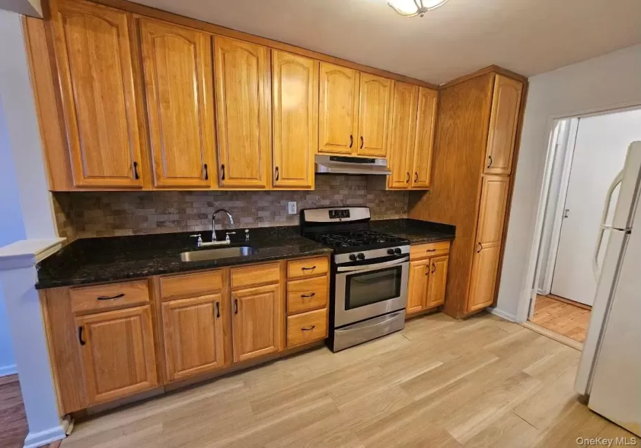 Kitchen featuring stainless steel gas range, dark stone counters, freestanding refrigerator, light wood finished floors, and brown cabinets Kitchen featuring stainless steel gas range, dark stone counters, freestanding refrigerator, light wood finished floors, and brown cabinets