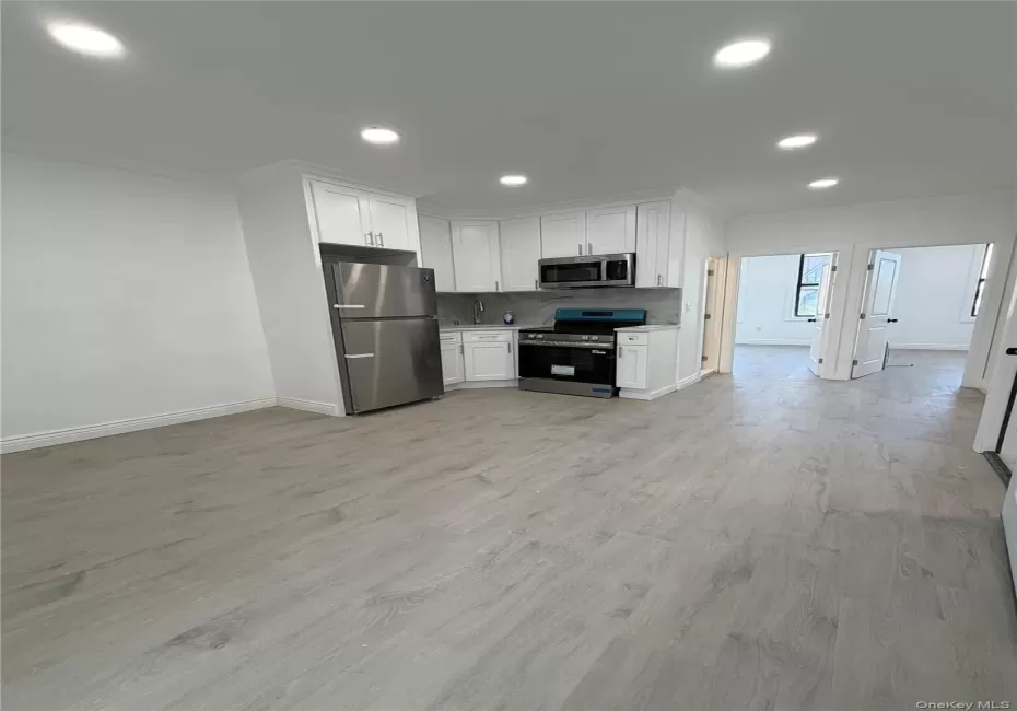 open living space Modern kitchen featuring white cabinetry, stainless steel appliances, and a light-toned countertop with matching backsplash open living space Modern kitchen featuring white cabinetry, stainless steel appliances, and a light-toned countertop with matching backsplash