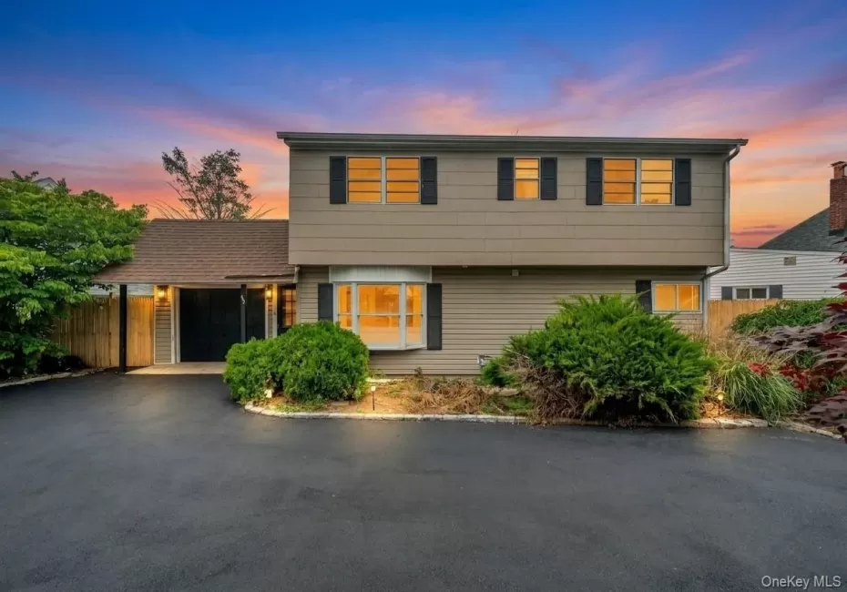 Multi-level residence featuring a bay window, dark shutters, and a prominent asphalt driveway Multi-level residence featuring a bay window, dark shutters, and a prominent asphalt driveway