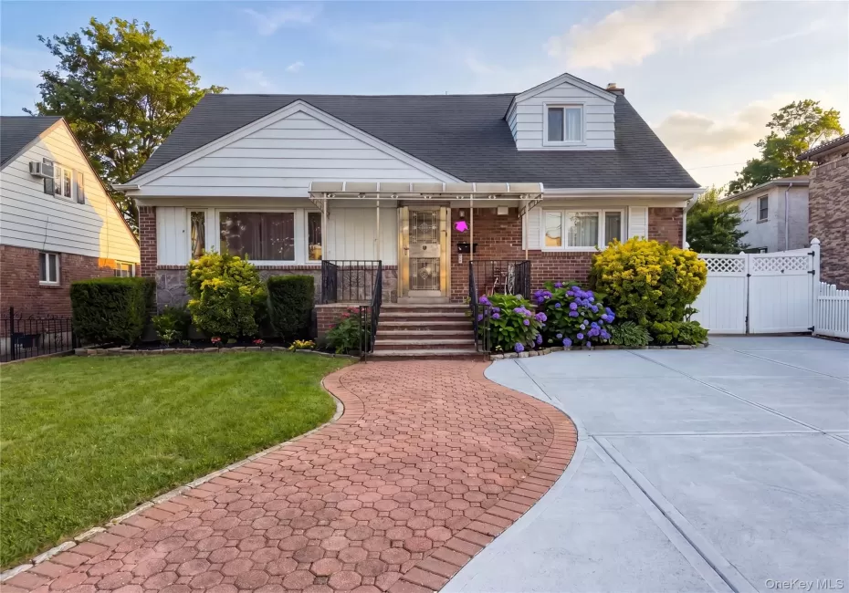 Brick and siding residence featuring a red paver walkway, mature landscaping, and a concrete driveway with a white privacy gate Brick and siding residence featuring a red paver walkway, mature landscaping, and a concrete driveway with a white privacy gate