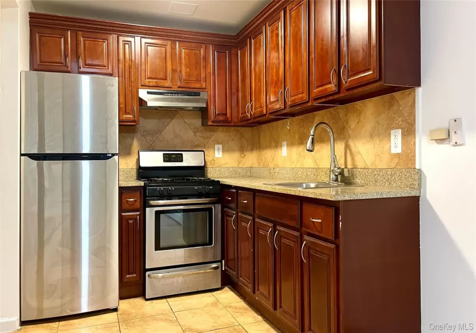 Kitchen with stainless steel appliances, light stone countertops, decorative backsplash, under cabinet range hood, and light tile patterned floors Kitchen with stainless steel appliances, light stone countertops, decorative backsplash, under cabinet range hood, and light tile patterned floors