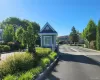 Entry gatehouse featuring a shingle roof and siding, surrounded by mature landscaping and paved roadways Entry gatehouse featuring a shingle roof and siding, surrounded by mature landscaping and paved roadways
