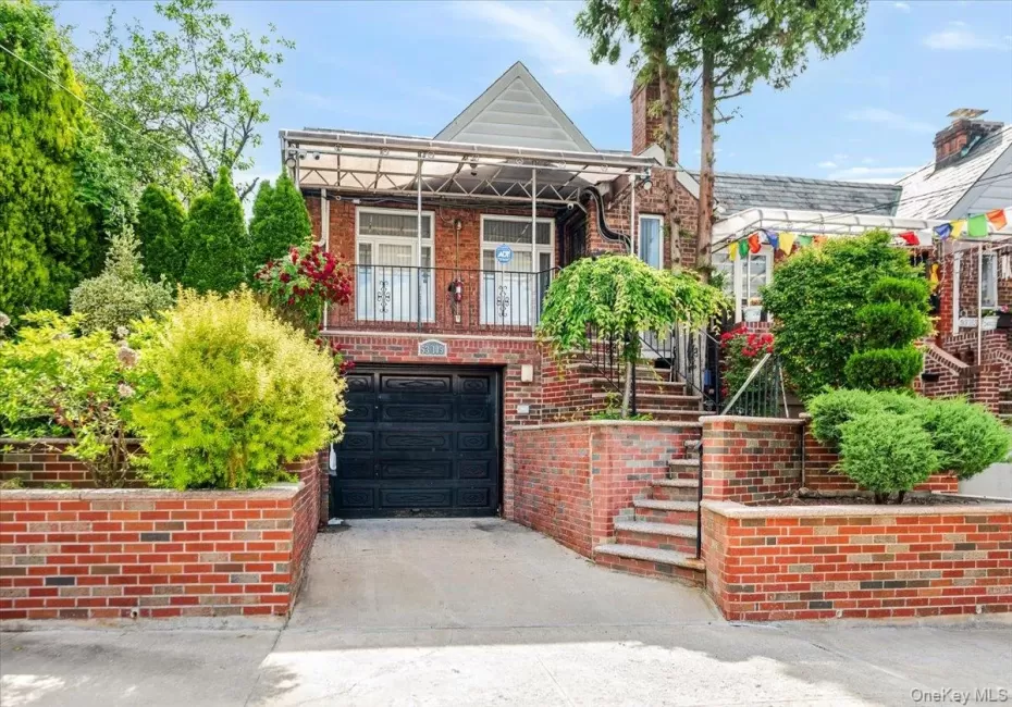 Brick exterior with a covered balcony featuring iron railings, an integrated garage, a brick staircase, and established landscaping Brick exterior with a covered balcony featuring iron railings, an integrated garage, a brick staircase, and established landscaping
