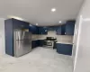Kitchen featuring blue shaker-style cabinetry, stainless steel appliances, light-toned countertops, and a full tile backsplash Kitchen featuring blue shaker-style cabinetry, stainless steel appliances, light-toned countertops, and a full tile backsplash