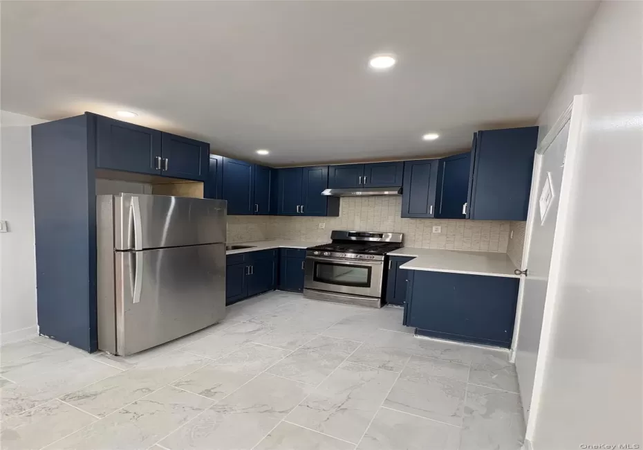 Kitchen featuring blue shaker-style cabinetry, stainless steel appliances, light-toned countertops, and a full tile backsplash Kitchen featuring blue shaker-style cabinetry, stainless steel appliances, light-toned countertops, and a full tile backsplash