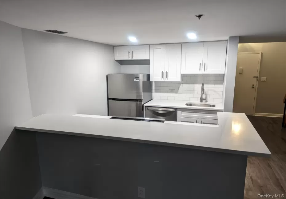 Contemporary kitchen featuring white shaker cabinetry, stainless steel appliances, a subway tile backsplash, and light-tone countertops Contemporary kitchen featuring white shaker cabinetry, stainless steel appliances, a subway tile backsplash, and light-tone countertops