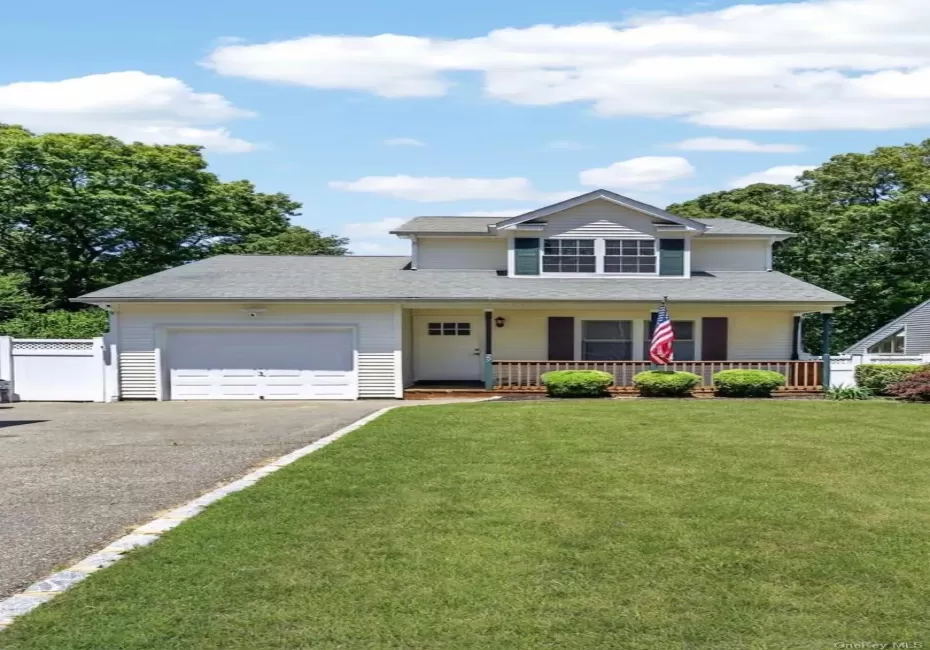 Two-story residence featuring a front porch with wood railing, an attached garage, a paved driveway, and a front lawn Two-story residence featuring a front porch with wood railing, an attached garage, a paved driveway, and a front lawn