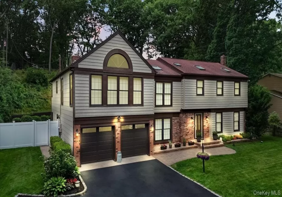 Two-story residence featuring light-toned siding with dark trim, a red-toned roofline with skylights, and a brick facade accent Two-story residence featuring light-toned siding with dark trim, a red-toned roofline with skylights, and a brick facade accent
