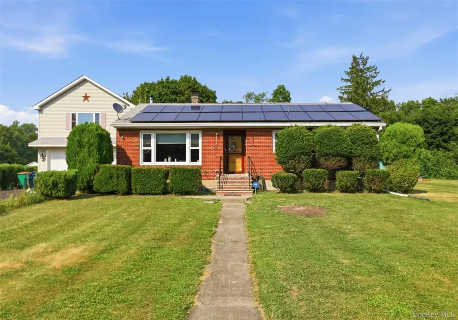 Brick facade home featuring solar panels and a landscaped front yard with a concrete walkway Brick facade home featuring solar panels and a landscaped front yard with a concrete walkway