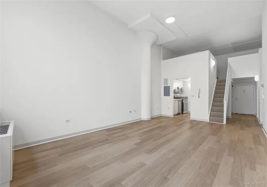Open-concept living space featuring wood-finish flooring, high ceilings, a prominent structural column, and a modern staircase with a carpet runner Open-concept living space featuring wood-finish flooring, high ceilings, a prominent structural column, and a modern staircase with a carpet runner