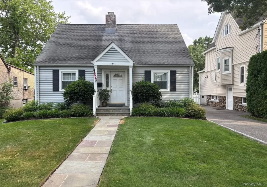 Charming Cape Cod residence featuring light blue siding, a dark shingle roof, and a prominent brick chimney Charming Cape Cod residence featuring light blue siding, a dark shingle roof, and a prominent brick chimney