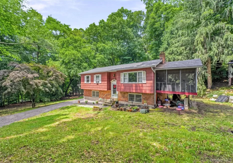 Raised ranch house featuring a red siding and brick facade, a screened-in porch, a paved driveway, and mature landscaping Raised ranch house featuring a red siding and brick facade, a screened-in porch, a paved driveway, and mature landscaping