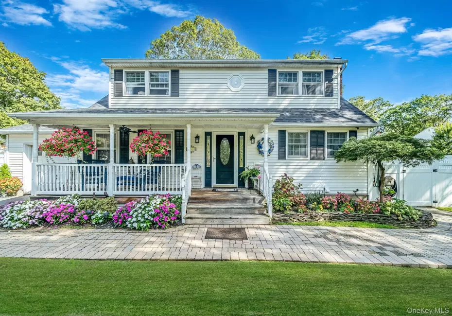 White siding exterior featuring a covered front porch with white railings, a paver walkway, mature landscaping, and a dark front door with decorative glass White siding exterior featuring a covered front porch with white railings, a paver walkway, mature landscaping, and a dark front door with decorative glass