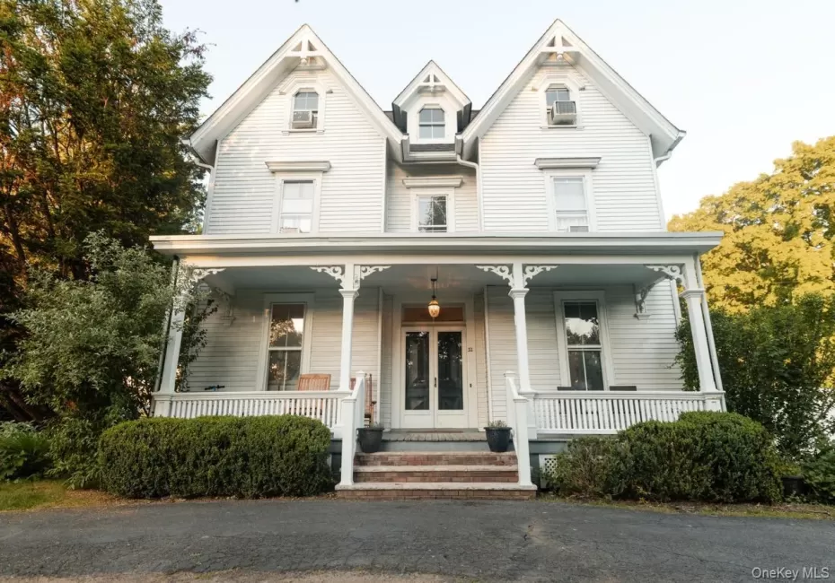 Classic white Victorian-style facade featuring multiple gables, a covered front porch with decorative brackets, a white spindle railing, and a central double-door entry with leaded glass Classic white Victorian-style facade featuring multiple gables, a covered front porch with decorative brackets, a white spindle railing, and a central double-door entry with leaded glass