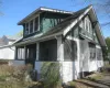 Craftsman-style home featuring a covered front porch, white shingle siding, green shake siding, a multi-gabled roofline, and visible window framing Craftsman-style home featuring a covered front porch, white shingle siding, green shake siding, a multi-gabled roofline, and visible window framing