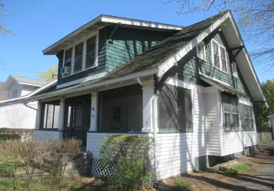 Craftsman-style home featuring a covered front porch, white shingle siding, green shake siding, a multi-gabled roofline, and visible window framing Craftsman-style home featuring a covered front porch, white shingle siding, green shake siding, a multi-gabled roofline, and visible window framing