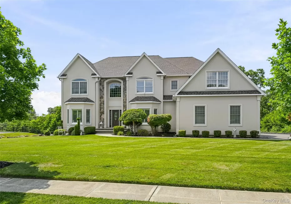 Stately two-story residence featuring a bay window, a prominent entry with a dark door, multiple windows, a sidewalk, and a manicured lawn Stately two-story residence featuring a bay window, a prominent entry with a dark door, multiple windows, a sidewalk, and a manicured lawn
