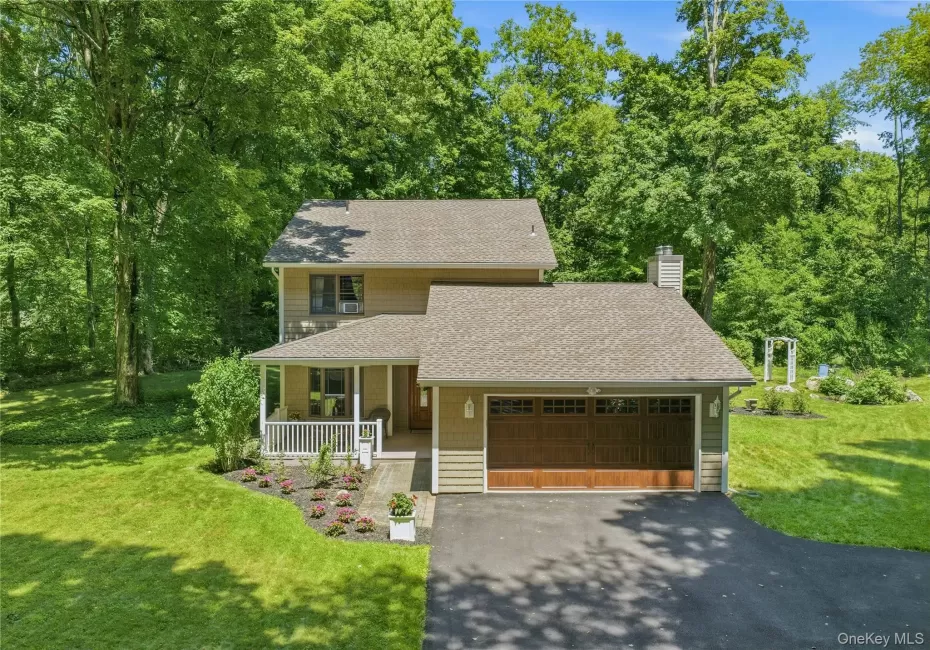 Two-story residence featuring siding exterior, an attached garage with a wood-finish door, and a covered front porch with white railings Two-story residence featuring siding exterior, an attached garage with a wood-finish door, and a covered front porch with white railings