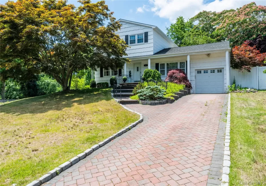 White two-story residence featuring a front-facing garage, a brick paver driveway, and a covered porch entry. White two-story residence featuring a front-facing garage, a brick paver driveway, and a covered porch entry.