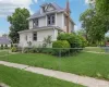 Traditional Colonial revival foursquare-style residence featuring light-colored siding, a dark shingle roof, and a prominent brick chimney Traditional Colonial revival foursquare-style residence featuring light-colored siding, a dark shingle roof, and a prominent brick chimney