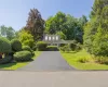 Front exterior with a paved driveway, manicured lawn, and mature trees Front exterior with a paved driveway, manicured lawn, and mature trees