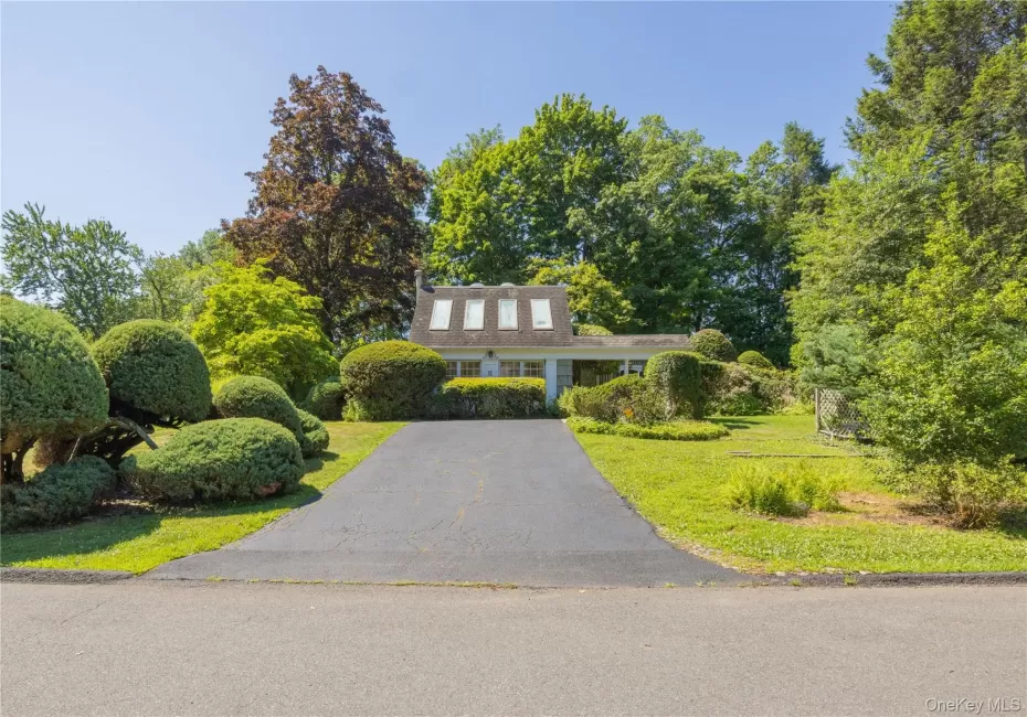 Front exterior with a paved driveway, manicured lawn, and mature trees Front exterior with a paved driveway, manicured lawn, and mature trees