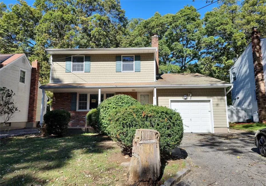 Traditional-style house featuring a garage, a chimney, a front lawn, driveway, and a porch Traditional-style house featuring a garage, a chimney, a front lawn, driveway, and a porch