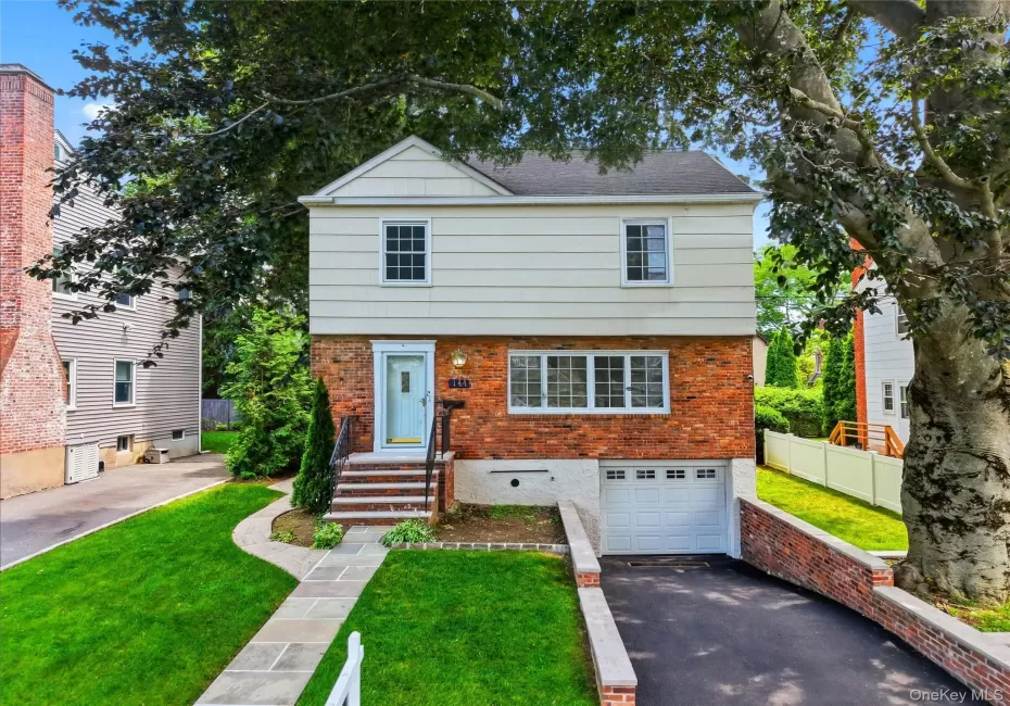 Brick and siding exterior featuring a light blue front door, an integrated garage, a stone walkway, a paved driveway, and established landscaping Brick and siding exterior featuring a light blue front door, an integrated garage, a stone walkway, a paved driveway, and established landscaping
