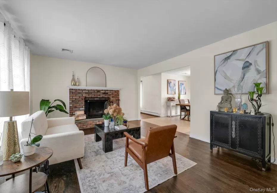 Living space with dark wood-finish flooring, a brick fireplace, and a large window Living space with dark wood-finish flooring, a brick fireplace, and a large window
