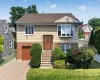Split-level home featuring brick and shingle siding, an attached garage with a brown door, and a paver driveway Split-level home featuring brick and shingle siding, an attached garage with a brown door, and a paver driveway