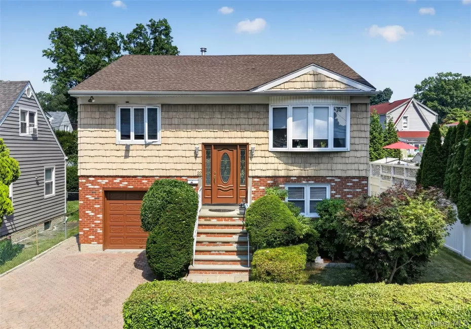 Split-level home featuring brick and shingle siding, an attached garage with a brown door, and a paver driveway Split-level home featuring brick and shingle siding, an attached garage with a brown door, and a paver driveway