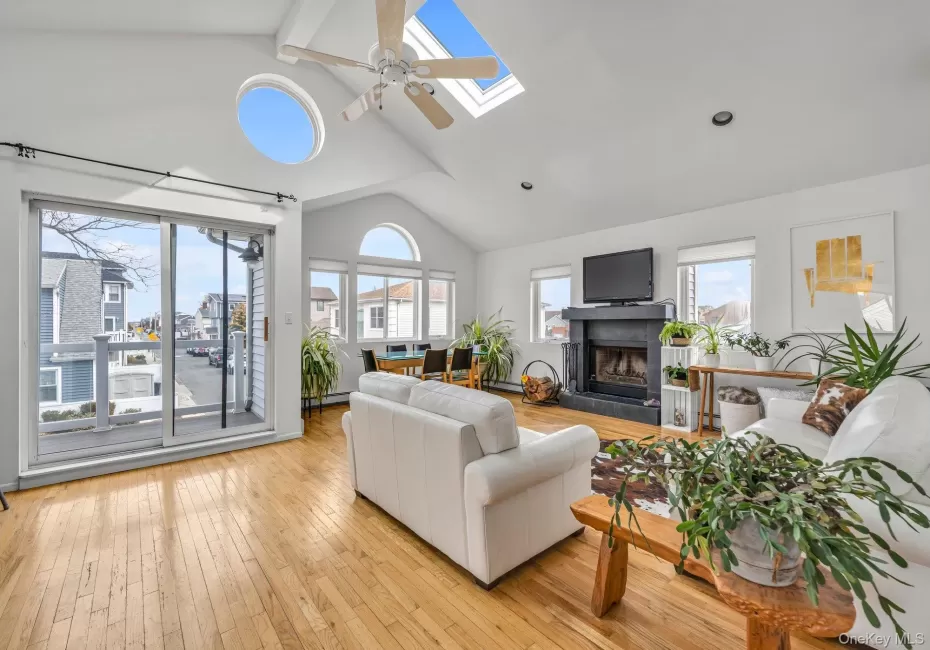 Living room with a ceiling fan, a skylight, light wood-type flooring, a fireplace with raised hearth, and baseboard heating Living room with a ceiling fan, a skylight, light wood-type flooring, a fireplace with raised hearth, and baseboard heating