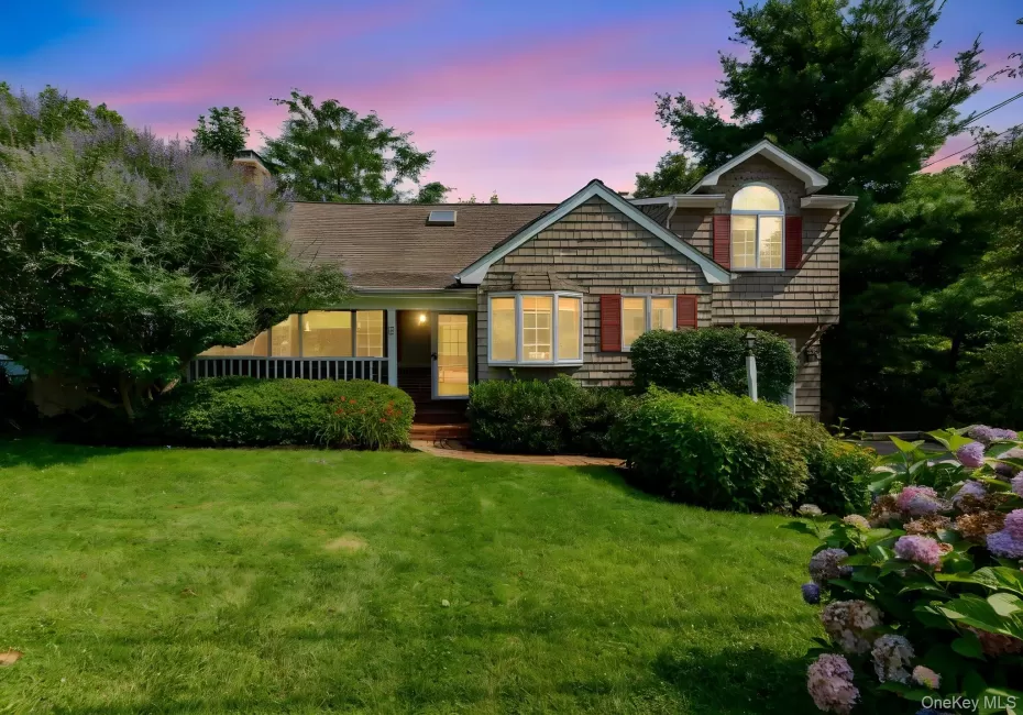 Shingle-sided residence featuring a covered porch with white railings, a bay window, and an upper-level arched window with red shutters Shingle-sided residence featuring a covered porch with white railings, a bay window, and an upper-level arched window with red shutters
