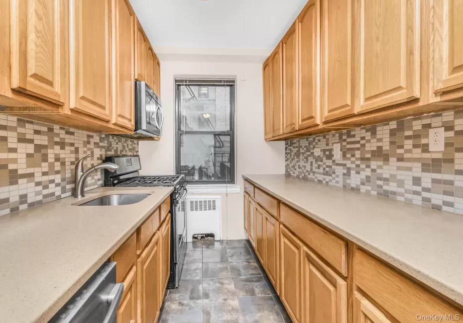 Kitchen featuring appliances with stainless steel finishes, decorative backsplash, radiator heating unit, and light stone counters Kitchen featuring appliances with stainless steel finishes, decorative backsplash, radiator heating unit, and light stone counters