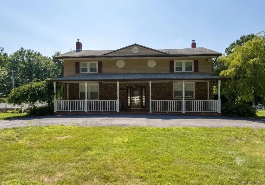 Two-story residence featuring a full-width front porch with white railing, brick and siding exterior, and a central double-door entry Two-story residence featuring a full-width front porch with white railing, brick and siding exterior, and a central double-door entry