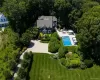 Expansive property featuring a dark-sided residence with white trim, a large in-ground swimming pool, a spacious patio area, a gravel driveway, and extensive mature landscaping Expansive property featuring a dark-sided residence with white trim, a large in-ground swimming pool, a spacious patio area, a gravel driveway, and extensive mature landscaping