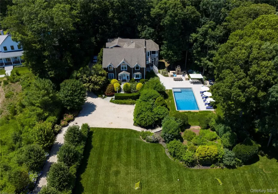 Expansive property featuring a dark-sided residence with white trim, a large in-ground swimming pool, a spacious patio area, a gravel driveway, and extensive mature landscaping Expansive property featuring a dark-sided residence with white trim, a large in-ground swimming pool, a spacious patio area, a gravel driveway, and extensive mature landscaping