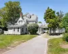 View of front facade with a balcony, a chimney, a front yard, gravel driveway, and a shingled roof View of front facade with a balcony, a chimney, a front yard, gravel driveway, and a shingled roof