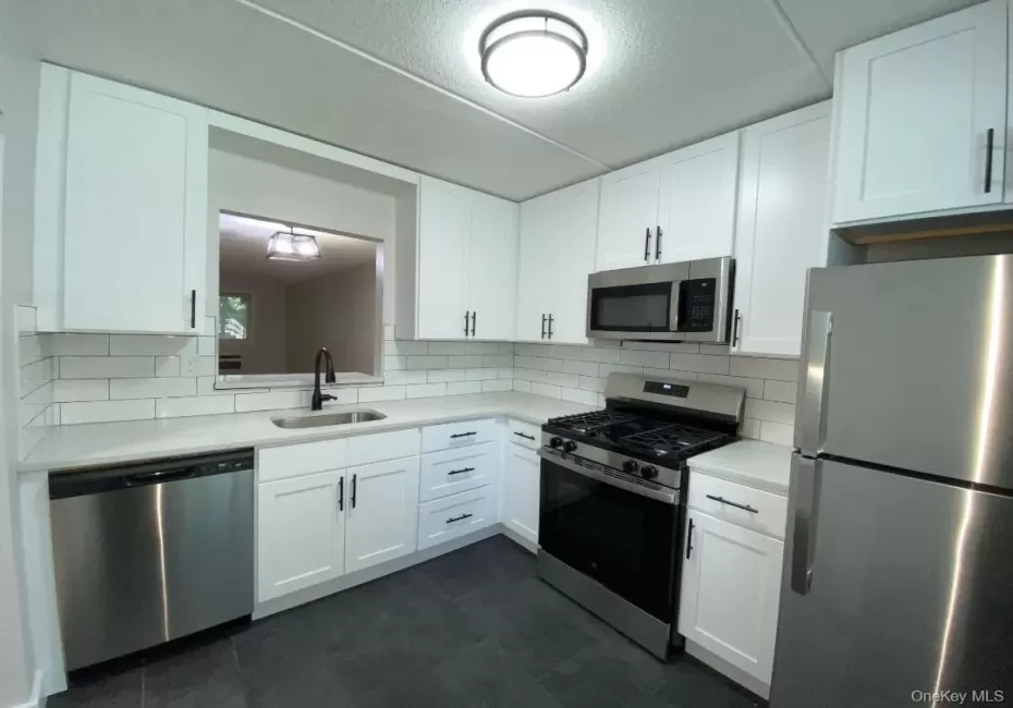 Beautifully renovated kitchen featuring white shaker cabinetry, quartz countertops, subway tile backsplash, stainless steel appliances and a ceramic tile floor Beautifully renovated kitchen featuring white shaker cabinetry, quartz countertops, subway tile backsplash, stainless steel appliances and a ceramic tile floor