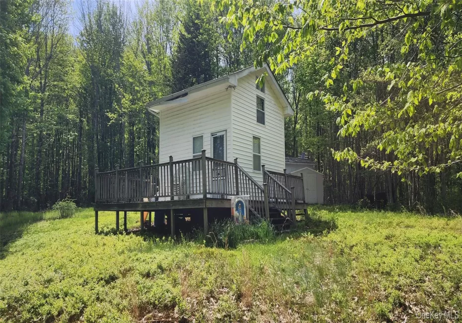 View of home's exterior with a storage unit, a wooden deck, an outdoor structure, and a view of trees View of home's exterior with a storage unit, a wooden deck, an outdoor structure, and a view of trees