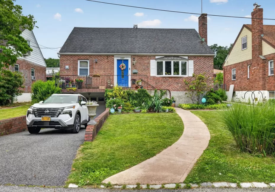 Brick exterior residence featuring a prominent bay window with white shutters, a distinctive blue entry door, and a dedicated driveway Brick exterior residence featuring a prominent bay window with white shutters, a distinctive blue entry door, and a dedicated driveway