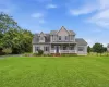 Two-story residence featuring a covered front porch, dormer windows, blue shutters, a dark blue front door, and a spacious front lawn Two-story residence featuring a covered front porch, dormer windows, blue shutters, a dark blue front door, and a spacious front lawn